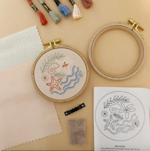 Embroidery hoop with starfish design, embroidery thread, and pattern sheet on a beige surface. 