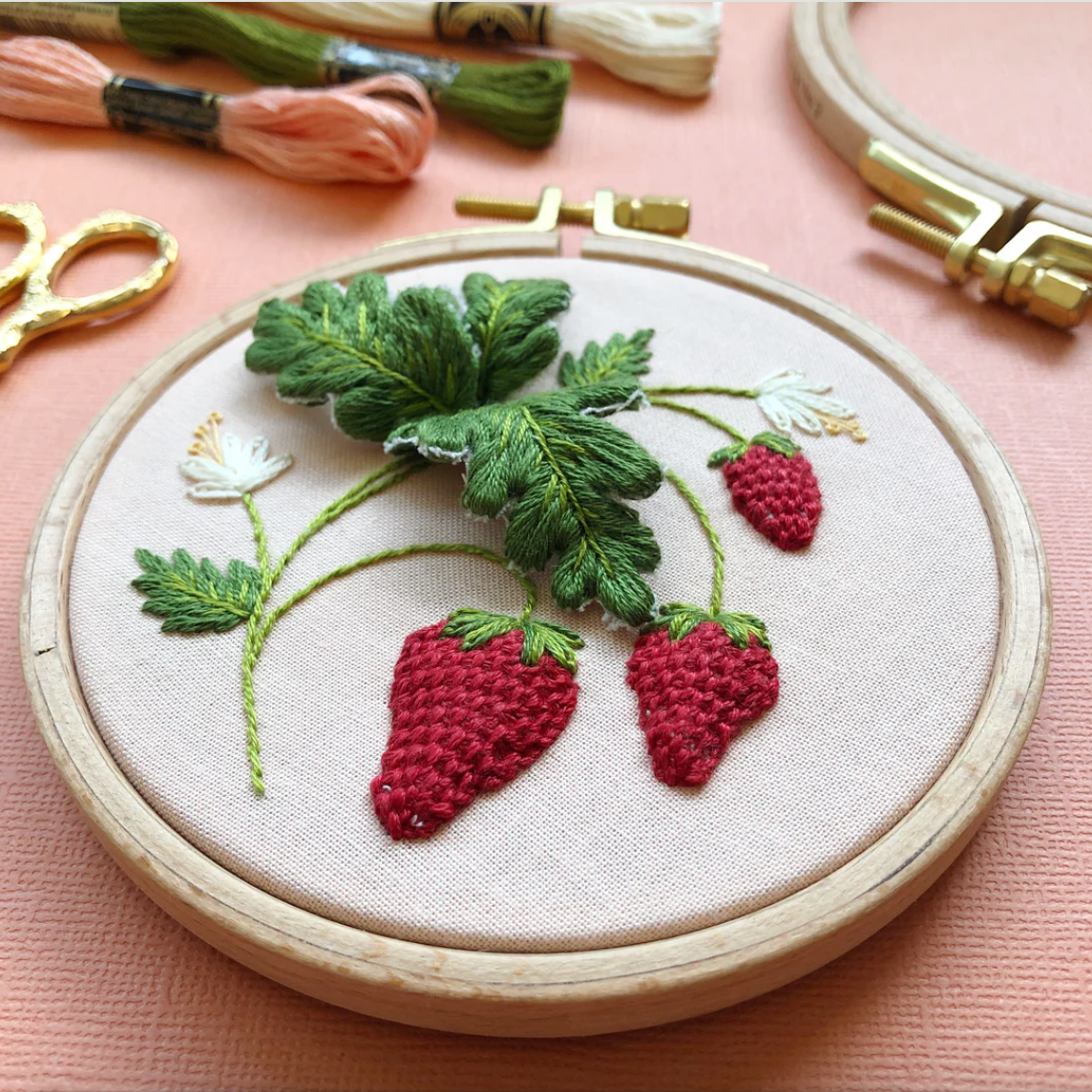 Embroidery hoop with embroidered strawberries and leaves on a pink background