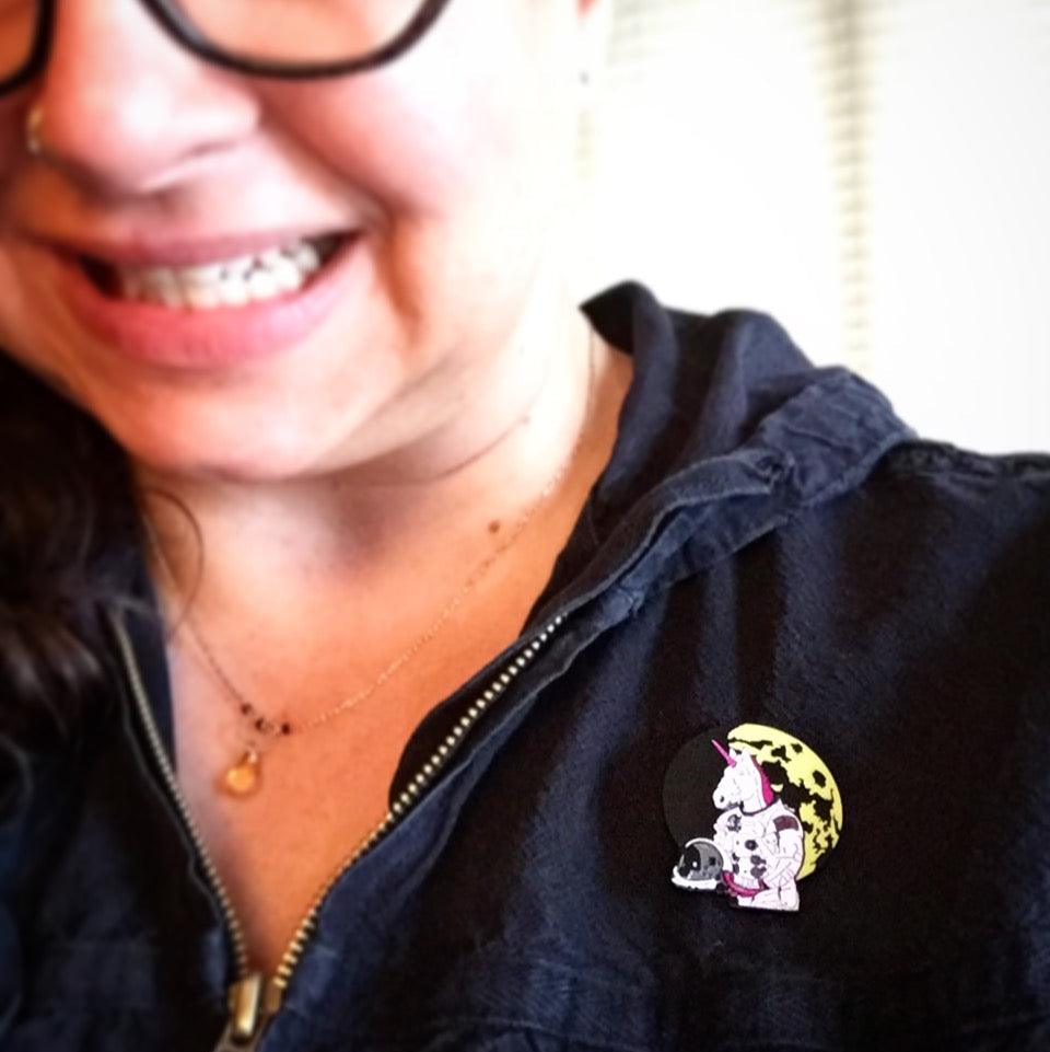 A close-up selfie of a person wearing a black zip-up hoodie with an Astronaut Unicorn pin on the chest.