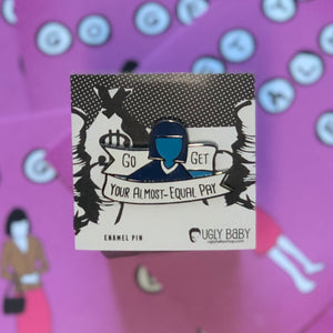 An enamel pin by Ugly Baby featuring a stylized blue and black illustration of a person holding a banner that reads 'Go GET YOUR ALMOST-EQUAL PAY', displayed on its white backing card against a pink background with cartoon graphics.