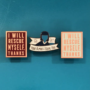 Three enamel pins displayed on a teal background. The left pin is square with a dark red background and rose gold text reading 'I WILL RESCUE MYSELF.