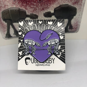 Heart shaped enamel pin called Love AT-AT First Sight with a purple glitter background. Shown on a backing card with hearts. 