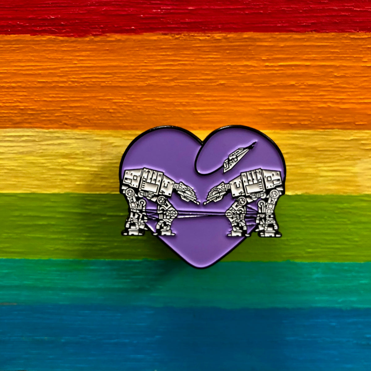 Heart shaped enamel pin called Love AT-AT First Sight with a purple background. Shown against a rainbow background.
