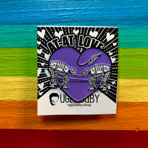 Heart shaped enamel pin called Love AT-AT First Sight with a purple background. Shown on a square paper background with black and white hearts. 
