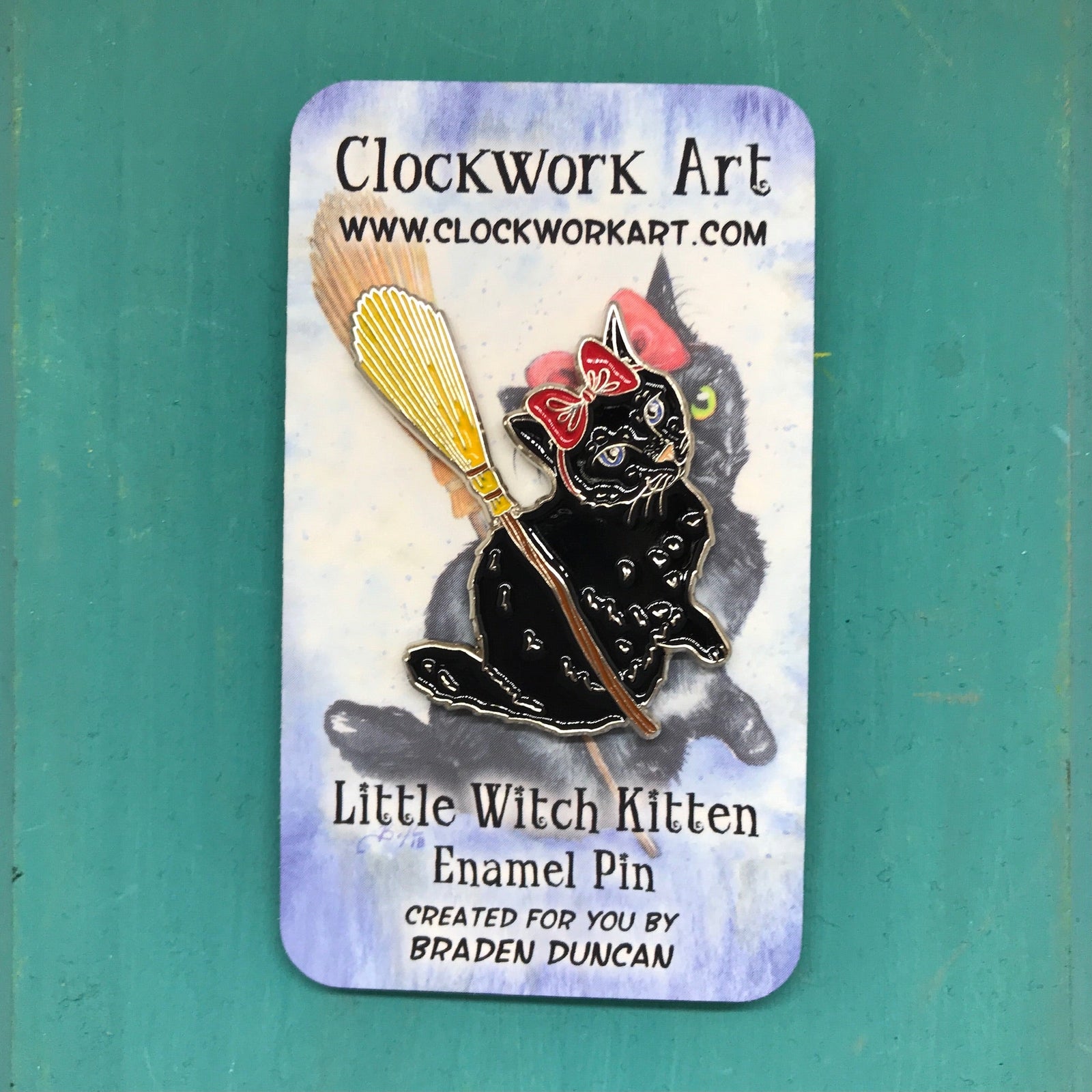 Enamel pin of a little witch cat with a big red bow riding a broom. 