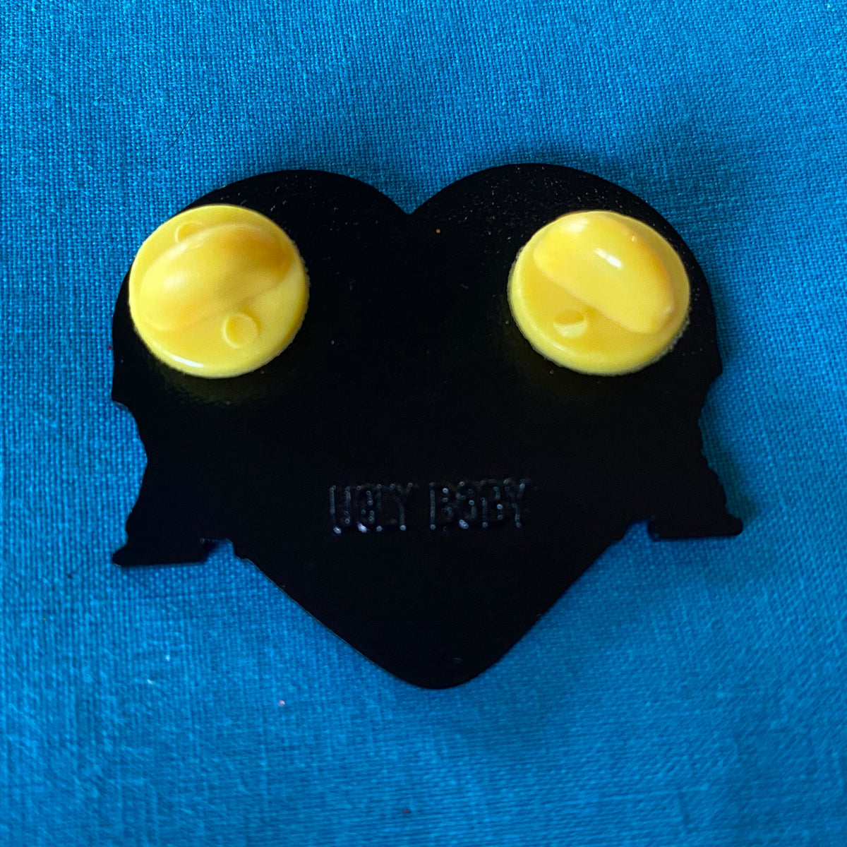 The back of a heart shaped enamel pin with two yellow rubber stoppers.