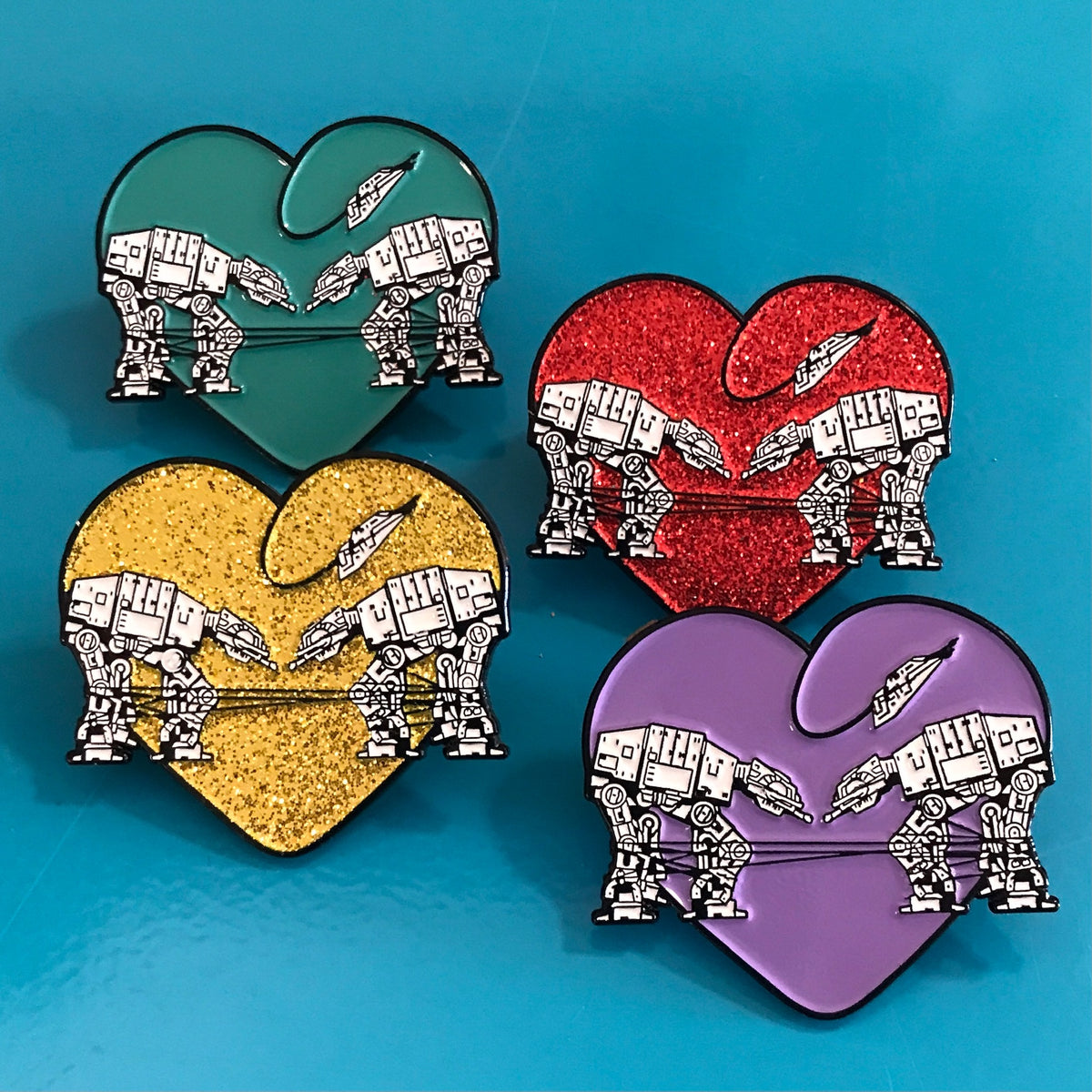 Group of four heart-shaped enamel pins called Love AT-AT First Sight in aqua, gold glitter, red glitter and purple.