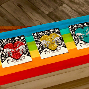 Three heart shaped enamel pins called Love AT-AT First Sight with a gold, red and aqua glitter backgrounds. Shown on backing cards with hearts. 