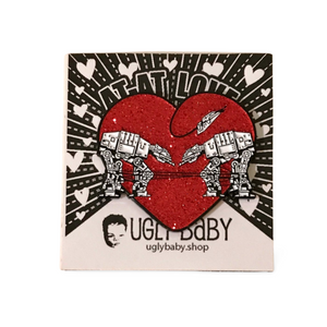 Heart shaped enamel pin called Love AT-AT First Sight with a red glitter background. Shown on a square paper background with black and white hearts. 
