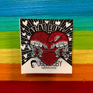 Heart shaped enamel pin called Love AT-AT First Sight with a red glitter background. Shown on a square paper background with black and white hearts. 