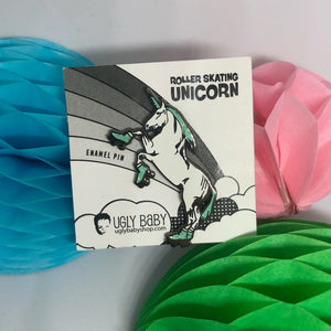 A small enamel pin card featuring a roller-skating unicorn illustration, placed on top of three honeycomb paper balls in blue, pink, and green. The card reads 'ROLLER SKATING UNICORN' and 'ENAMEL PIN,' with the brand 'UGLY BABY' visible at the bottom.