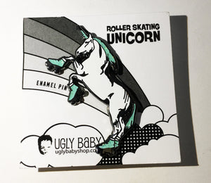 An pin featuring a roller-skating unicorn, mounted on its original white backing card. The backing card displays the text 'ROLLER SKATING UNICORN' and 'ENAMEL PIN' along with the brand 'UGLY BABY' and website 'uglybabyshop.