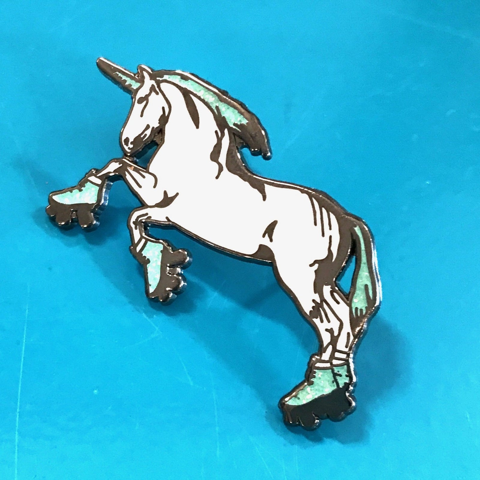 An enamel pin of a unicorn standing on hind legs and wearing roller skates. 