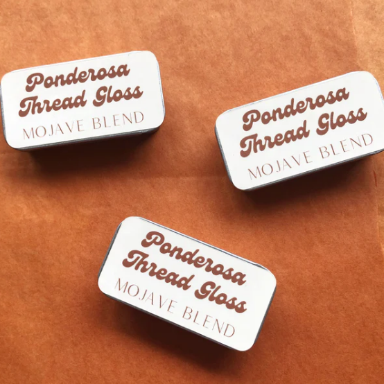 Three tins of Ponderosa Thread Gloss Mojave Blend on a brown leather surface.
