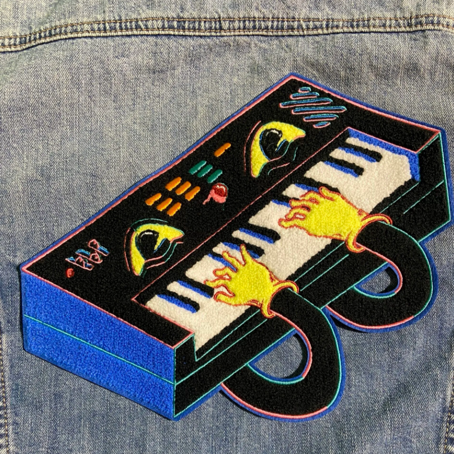 Embroidered patch of a cartoon keyboard playing itself on a denim jacket. 