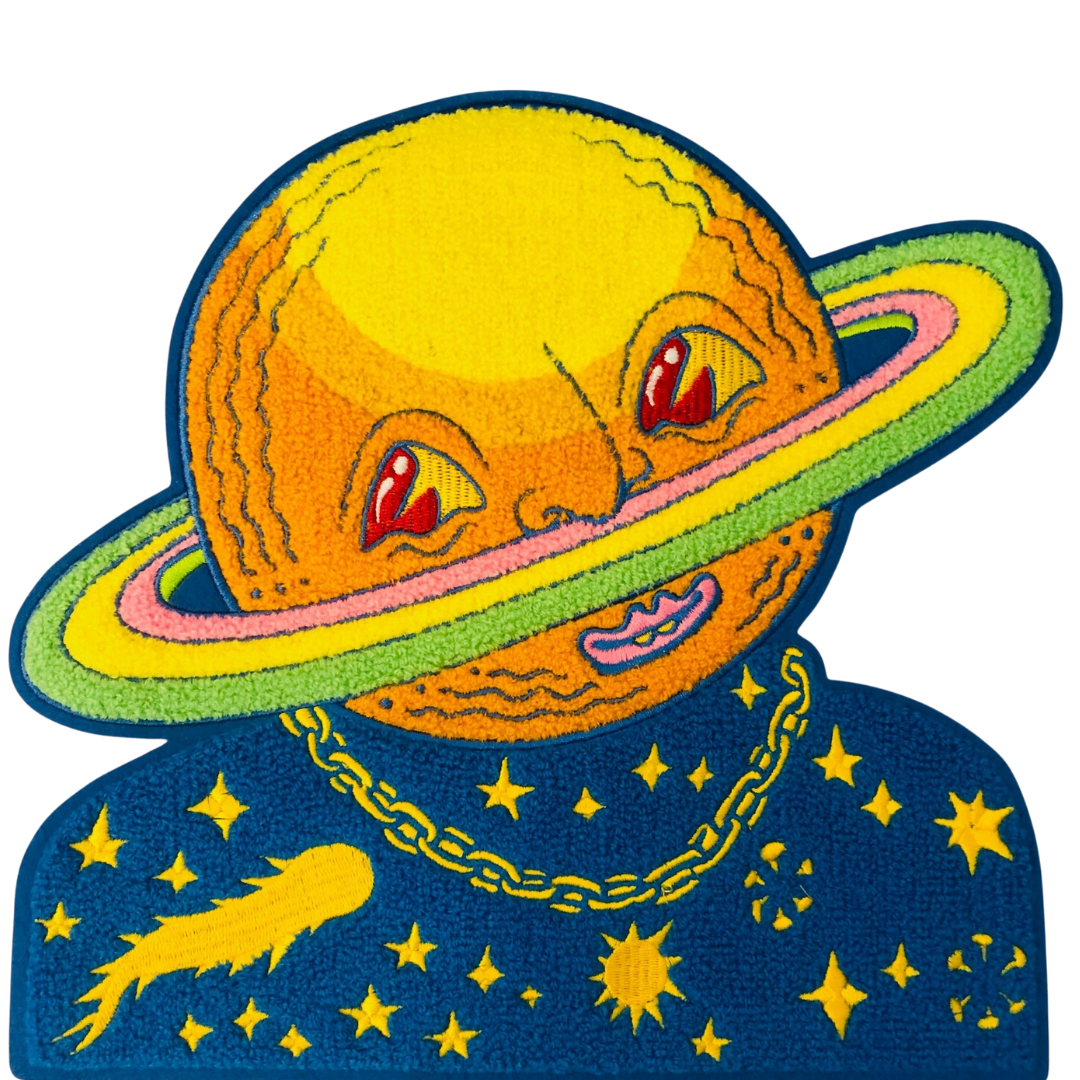 Embroidered patch of a Saturn planet with a face and rings on a blue background with stars and a comet.
