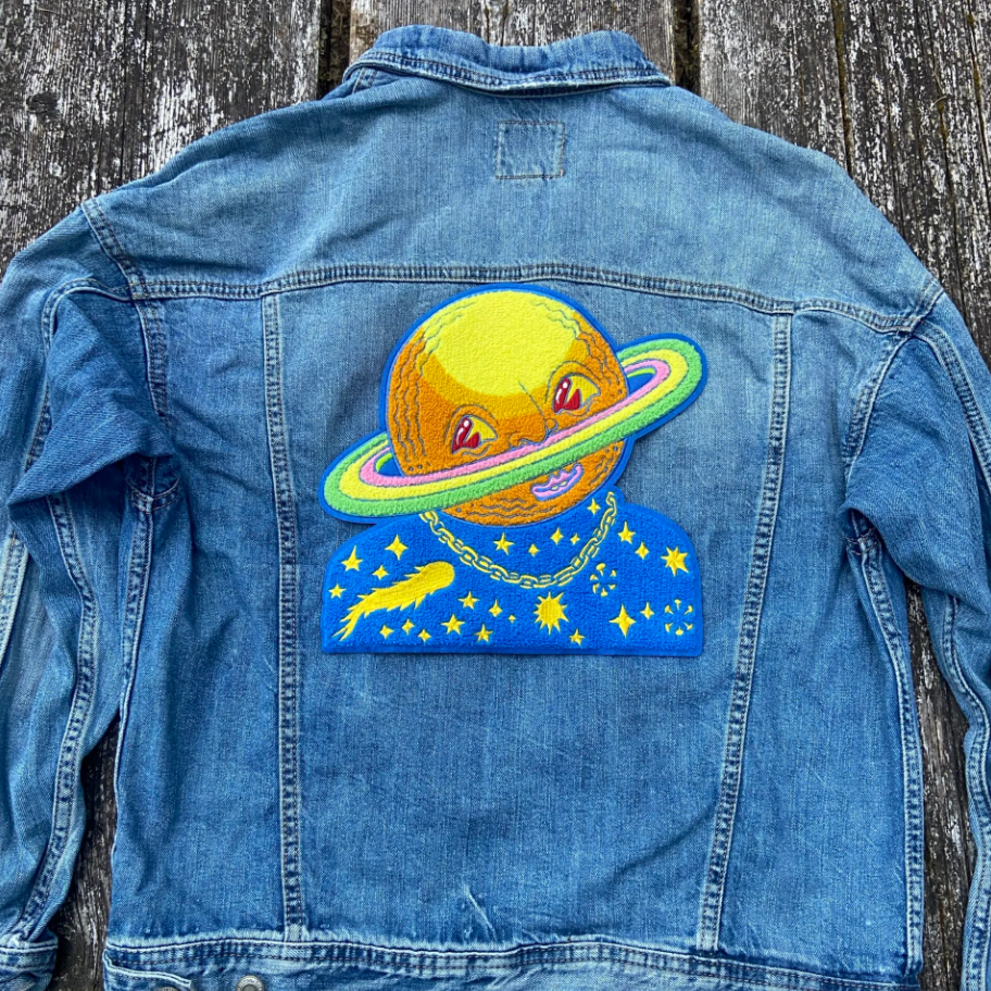 Blue denim jacket with a colorful Saturn planet patch on a wooden surface. 