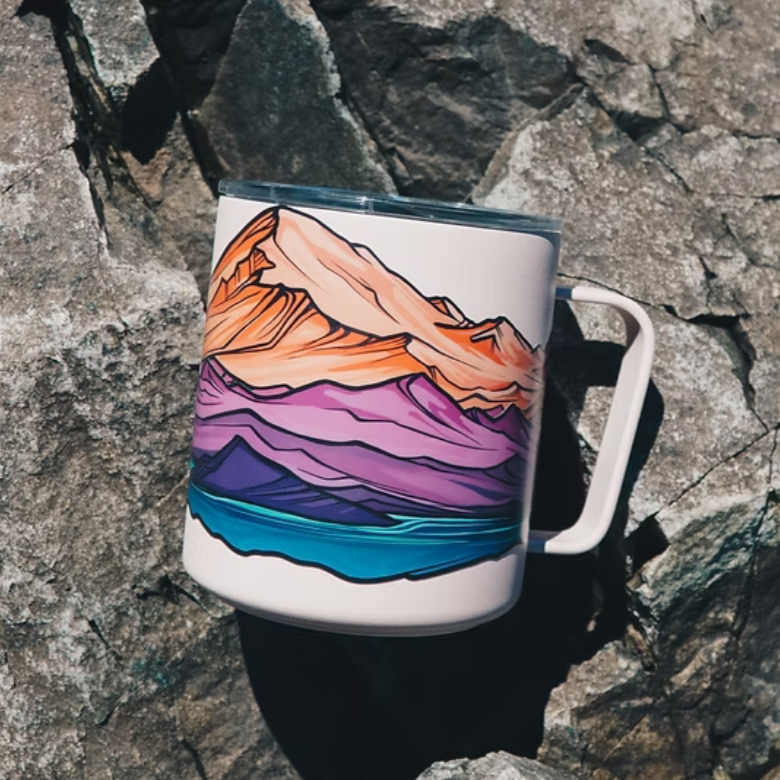 Colorful mug with a Mount Baker and Twin Sisters mountain design sticker. Mug is laying on a rocky surface