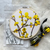 a completed dogwood embroidery kit is shown. The flowers are bright yellow. It sits atop a folded cloth with the pattern printed on it as well as a pack of embroidery floss with a ribbon tied around it. 