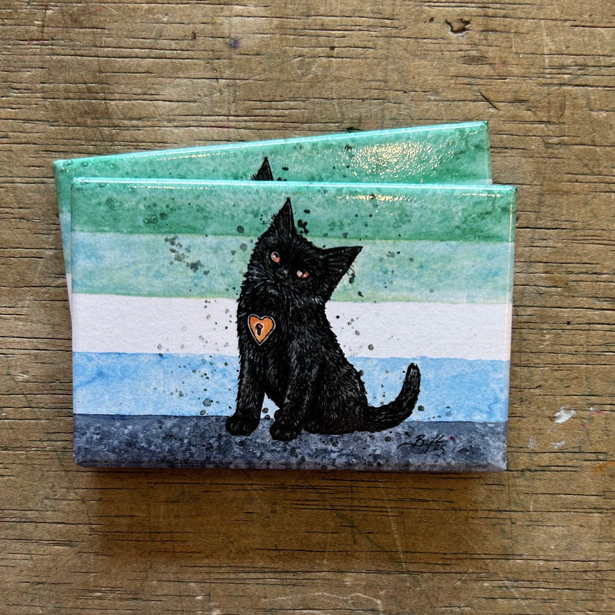 Magnet with a black cat illustration on a wooden surface. 