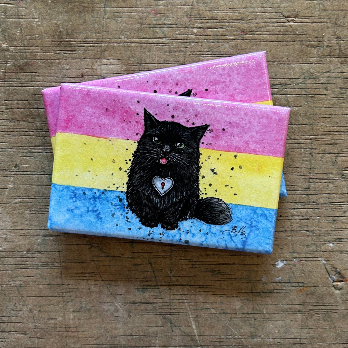 Two magnets with a black cat illustration on a wooden surface
