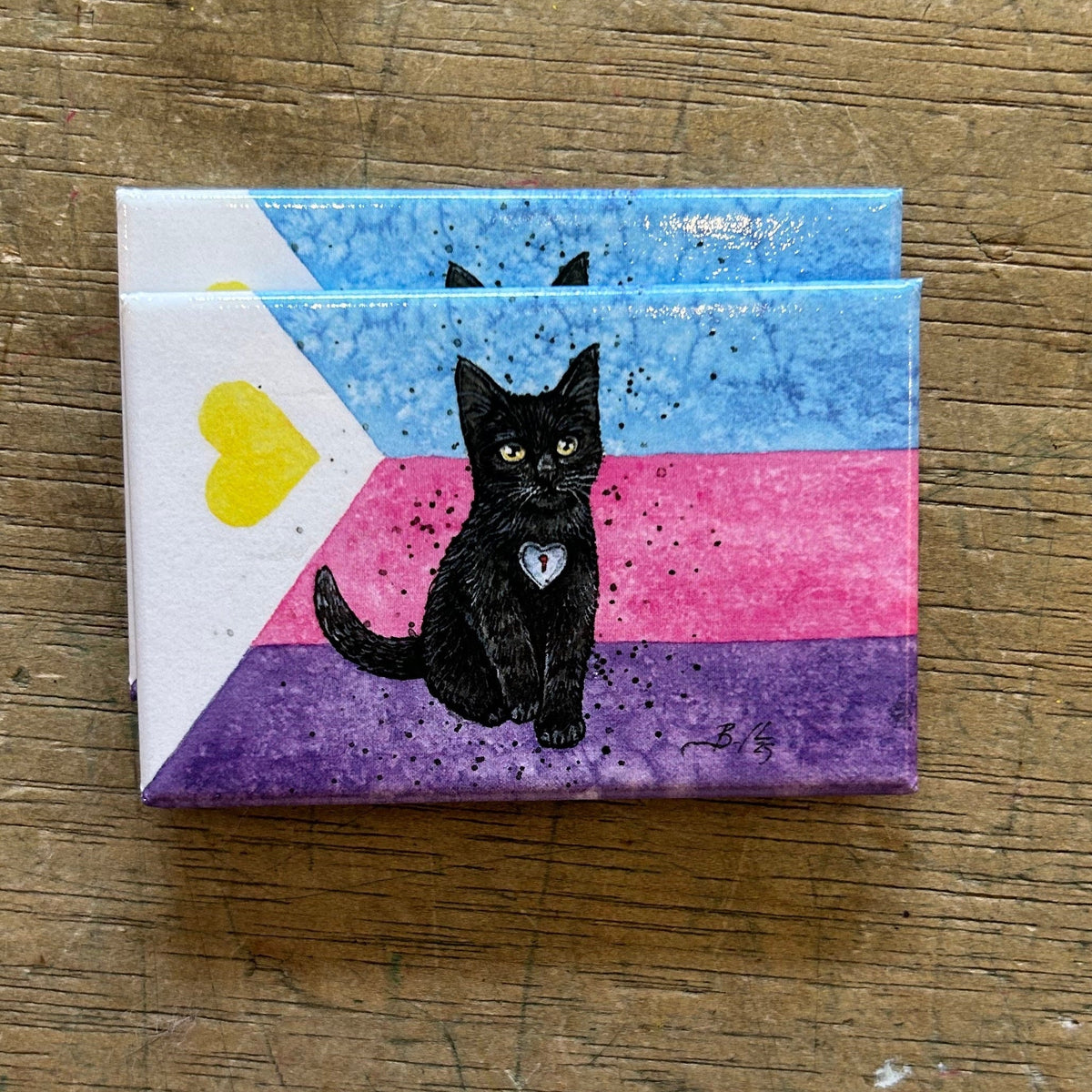 Magnet with a black cat illustration on a striped background, placed on a wooden surface.