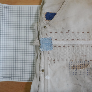 Worn jacket with patches on a wooden surface next to a piece of graph paper