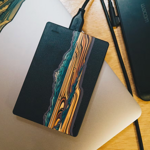 Black external hard drive with Puget Sound mini landscape sticker design on a wooden surface. 
