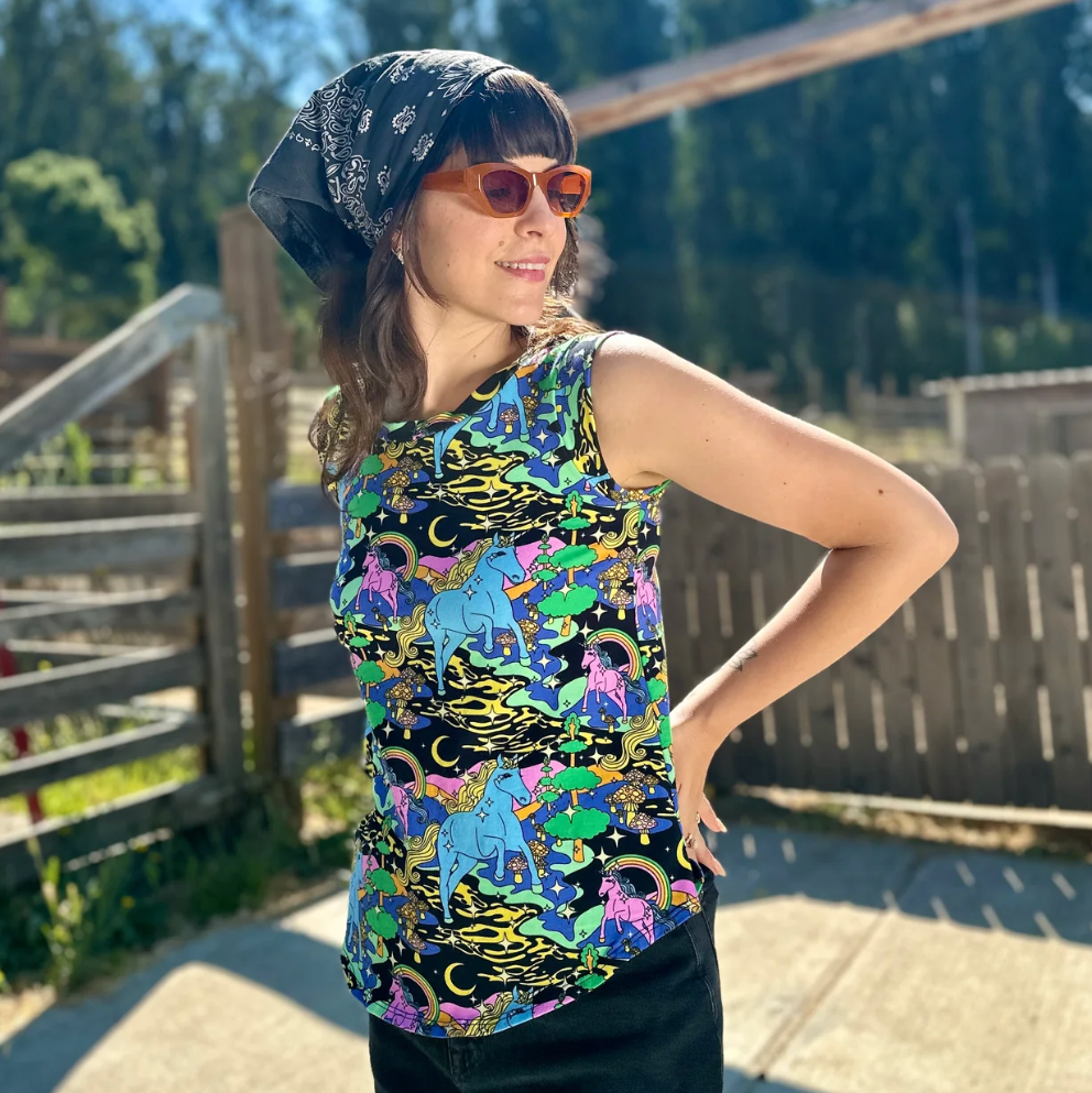 Woman wearing a colorful sleeveless shirt with unicorn pattern outdoors.