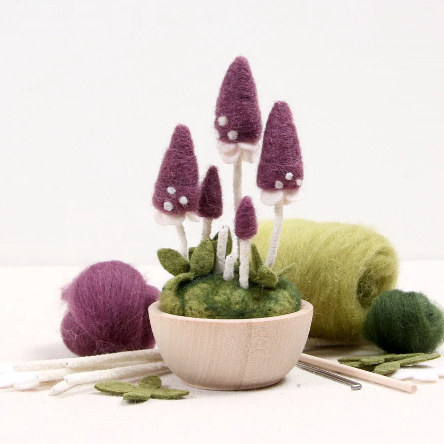 A completed Pixie Parasol mushroom needle felting kit shown with needle felting tools scattered on the white table. 
