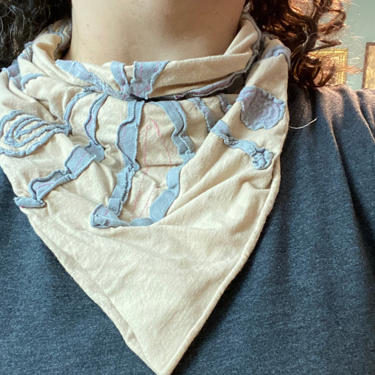 Example of a negative reverse applique bandana worn by a person. The bandana has a peach background with light gray foreground fabric and hot pink stitching.