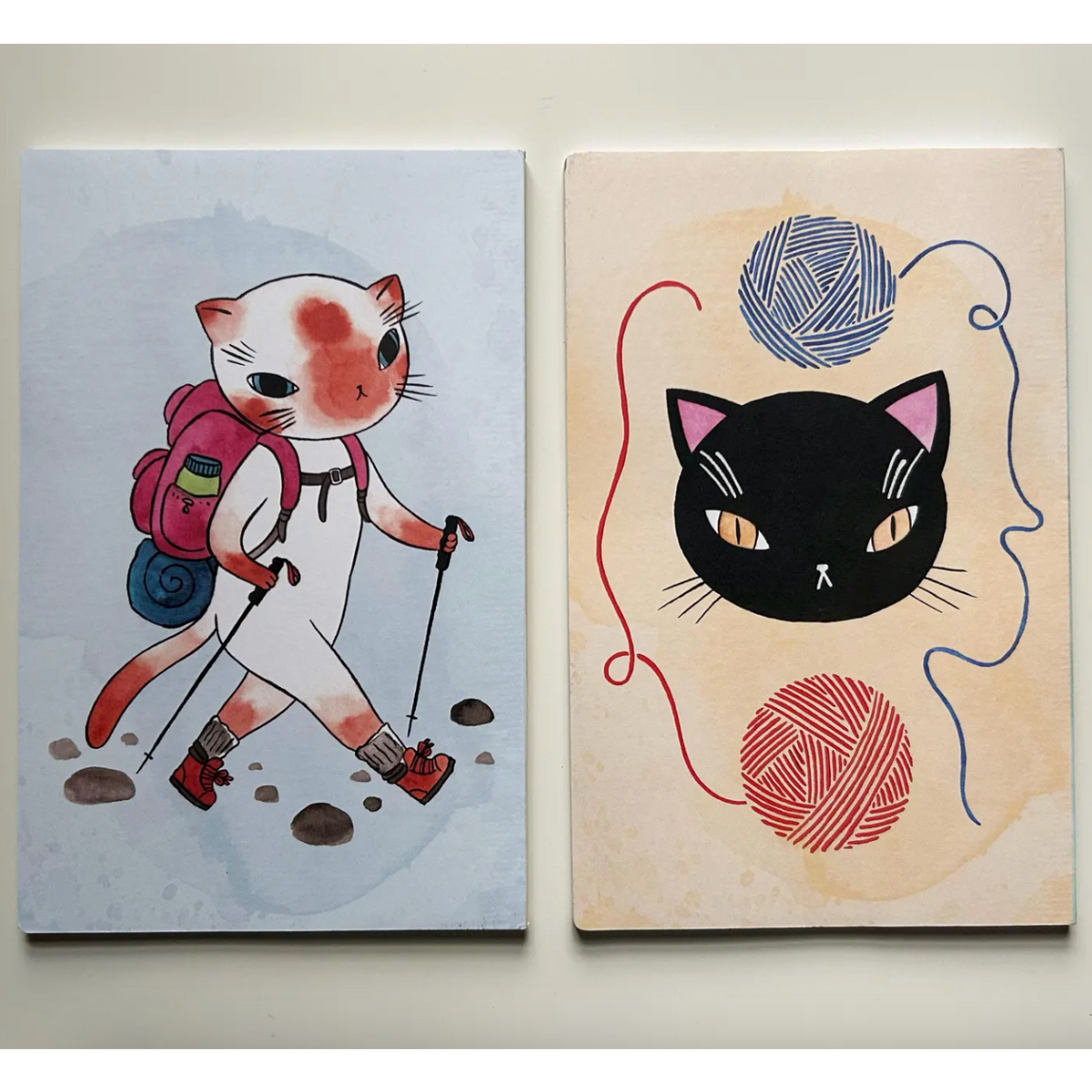 Two illustrations of cats, one with a backpack hiking and the other with yarn balls, on a light background.