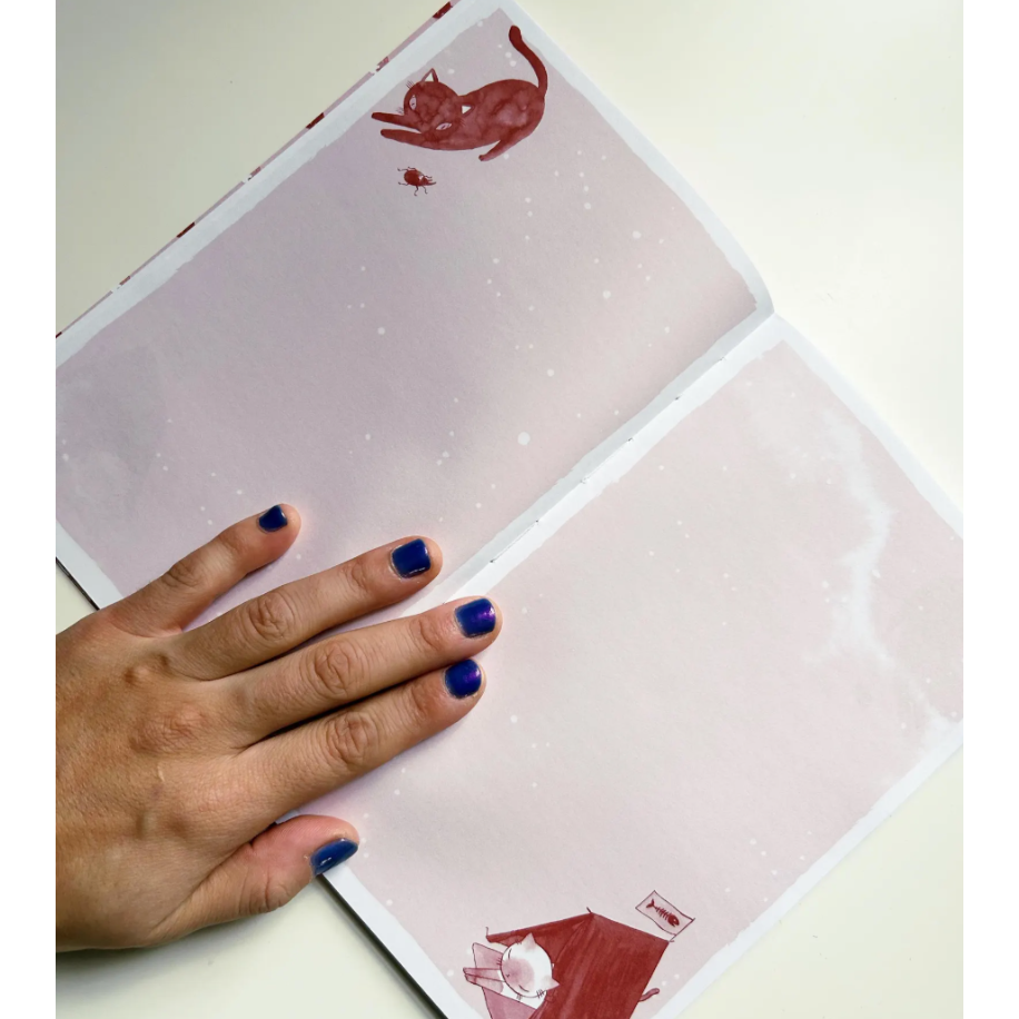 Two pages with red cat illustrations on a white surface, with a hand with blue nail polish holding one of them.
