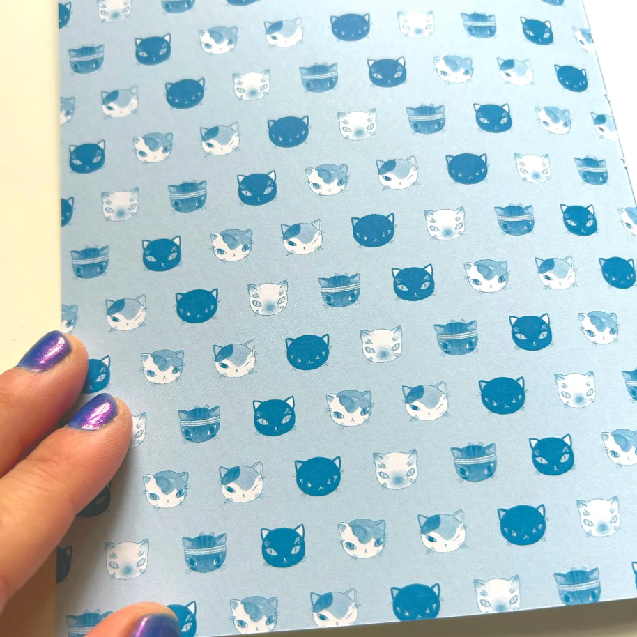 Sheet of paper with blue and white cat pattern held by a hand.