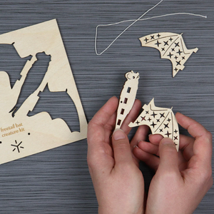 Wooden cut-out shapes of a bat on a textured surface with hands holding one of the shapes.