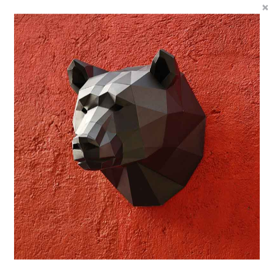 An example of a completed paper craft bear kit. It is a bear head hanging on a textured red wall.