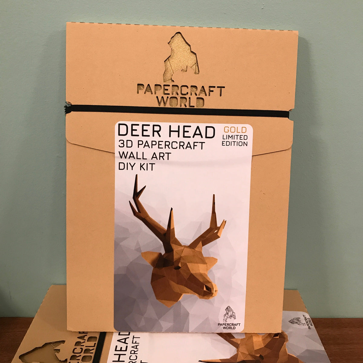 Packaging for the gold deer hear. It is kraft colored and has the papercraft world logo laser cut into the top. It has a picture of a completed gold deer head on the front.
