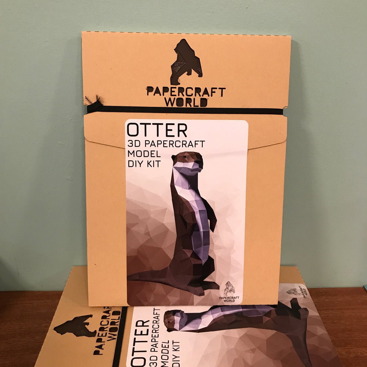 The packaging for the otter paper craft kit. It is kraft colored cardboard with the Papercraft World logo laser cut into the top.