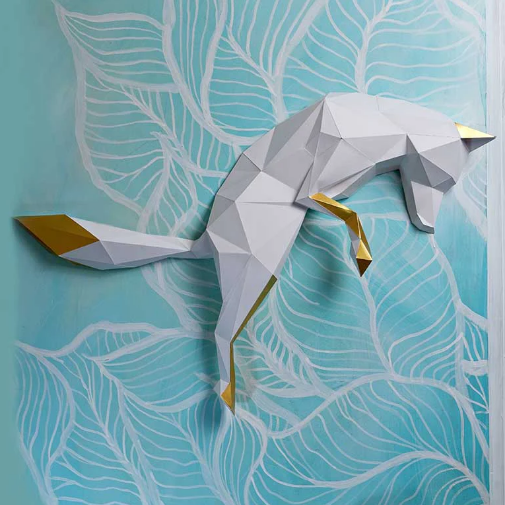 A completed example of the white pounding fox paper craft kit. It is hanging on a mint colored wall with white leaves painted on it.