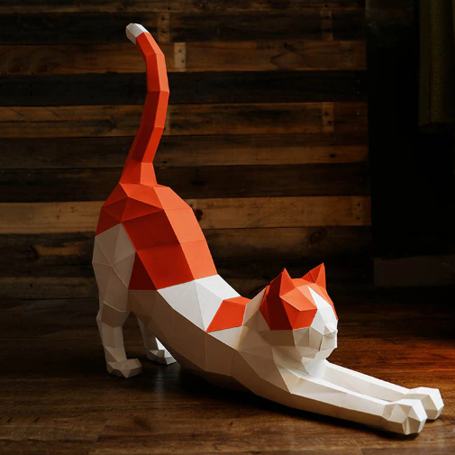 A completed example of a stretching cat paper craft kit. The cat is orange and white and is sitting on top of a wood table.