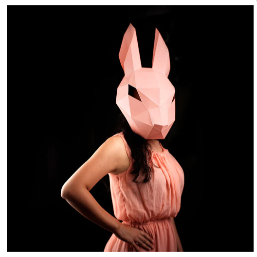 A person wearing a completed example of the bunny mask paper craft kit. They are wearing a peach colored dress that is a similar color to the mask.