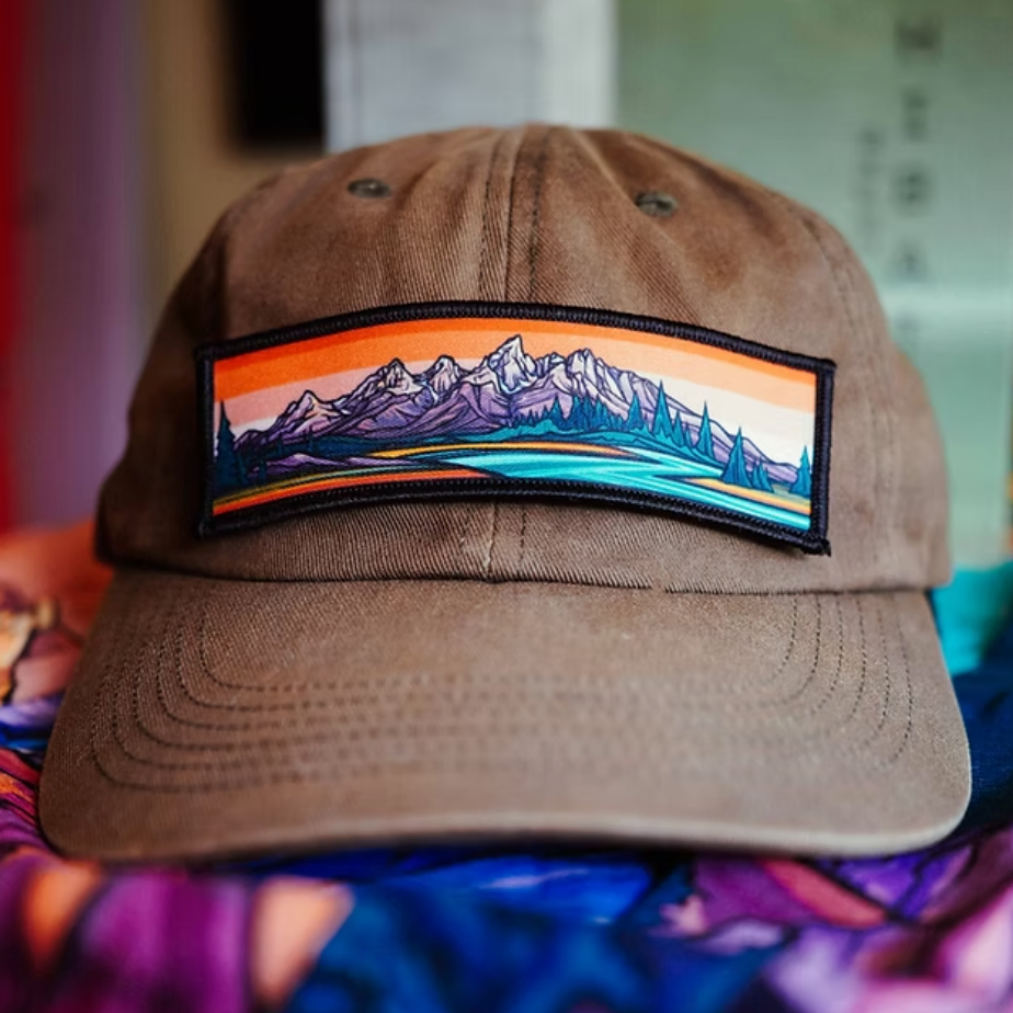 Brown cap with a mountain patch on a tan  fabric background