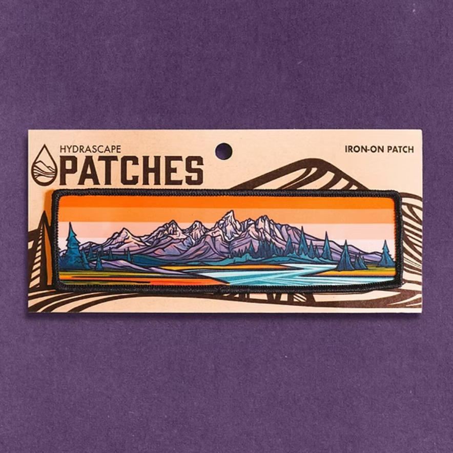 Iron-on patch with mountain landscape design on a purple background. 