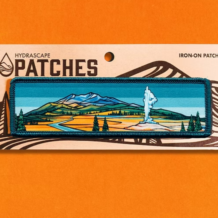 Iron-on patch with mountain and landscape design on a Hydrascape Patches card against an orange background. 