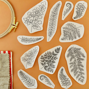 Set of embroidered leaf patterns on fabric with an embroidery hoop and fabric roll on a brown background. 