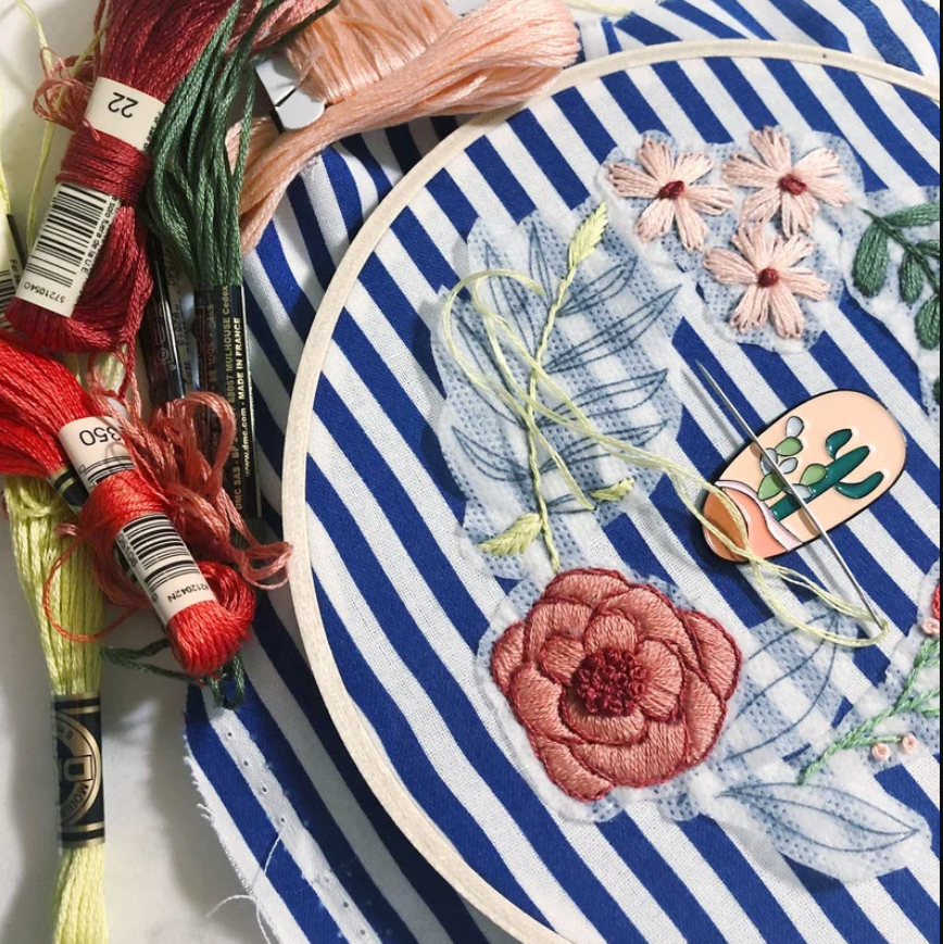Embroidery hoop with floral design and colorful threads on a striped fabric background.