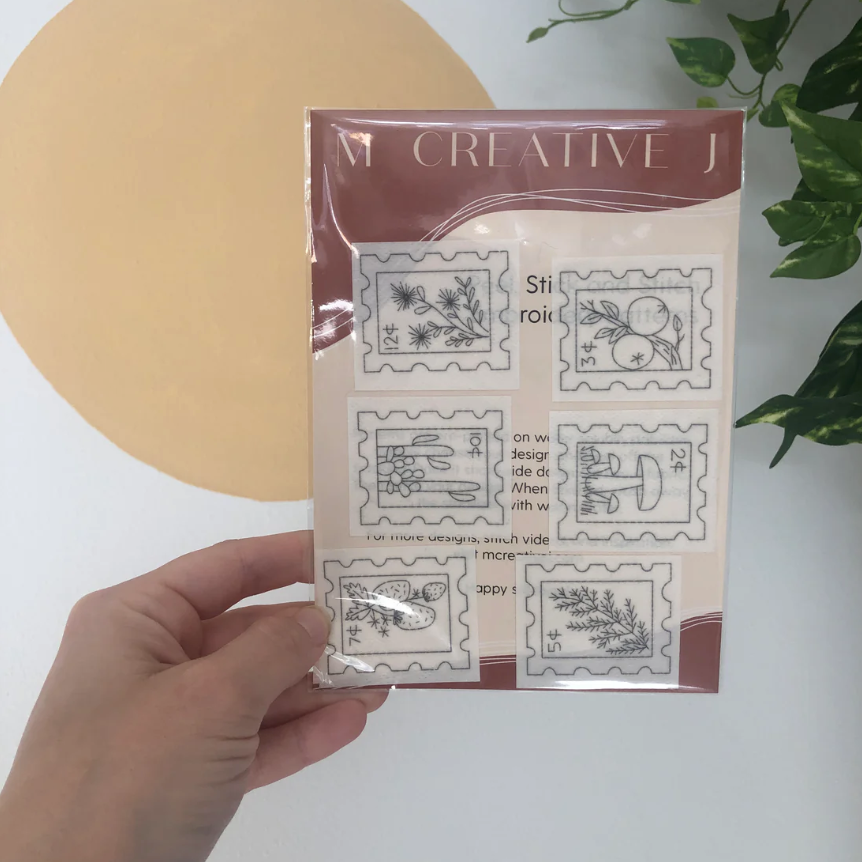 Hand holding a package of 'Creative J' stamps with floral designs on a white background.