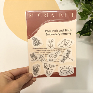Pack of peel, stick, and stitch embroidery patterns held by a hand with a plant in the background.
