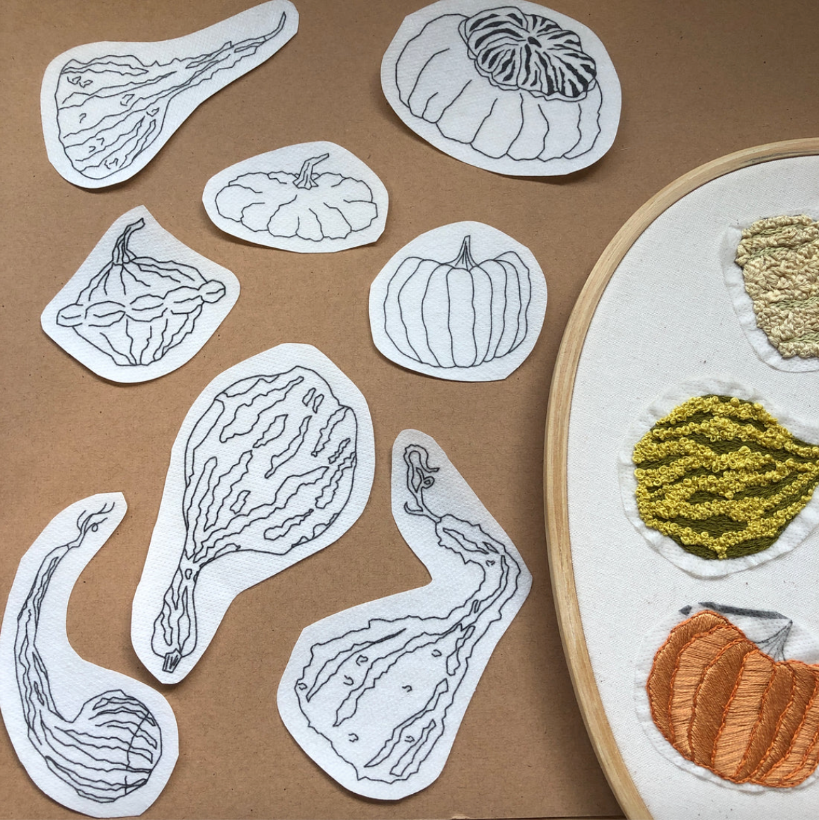 Embroidery patterns of pumpkins and gourds on a brown background with a completed embroidery piece.