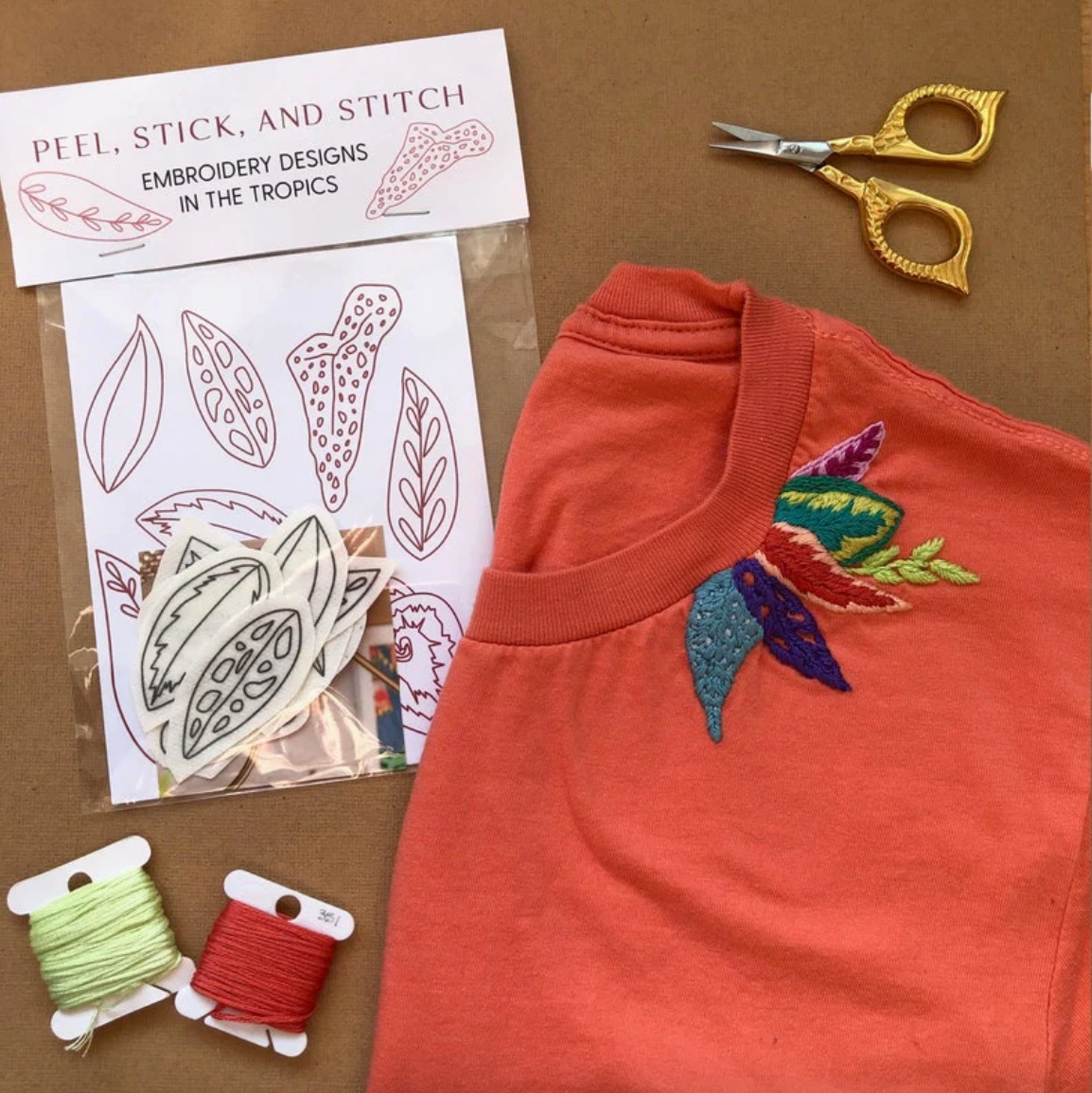 Embroidery kit with designs, thread, scissors, and embroidered shirt on a brown background. 